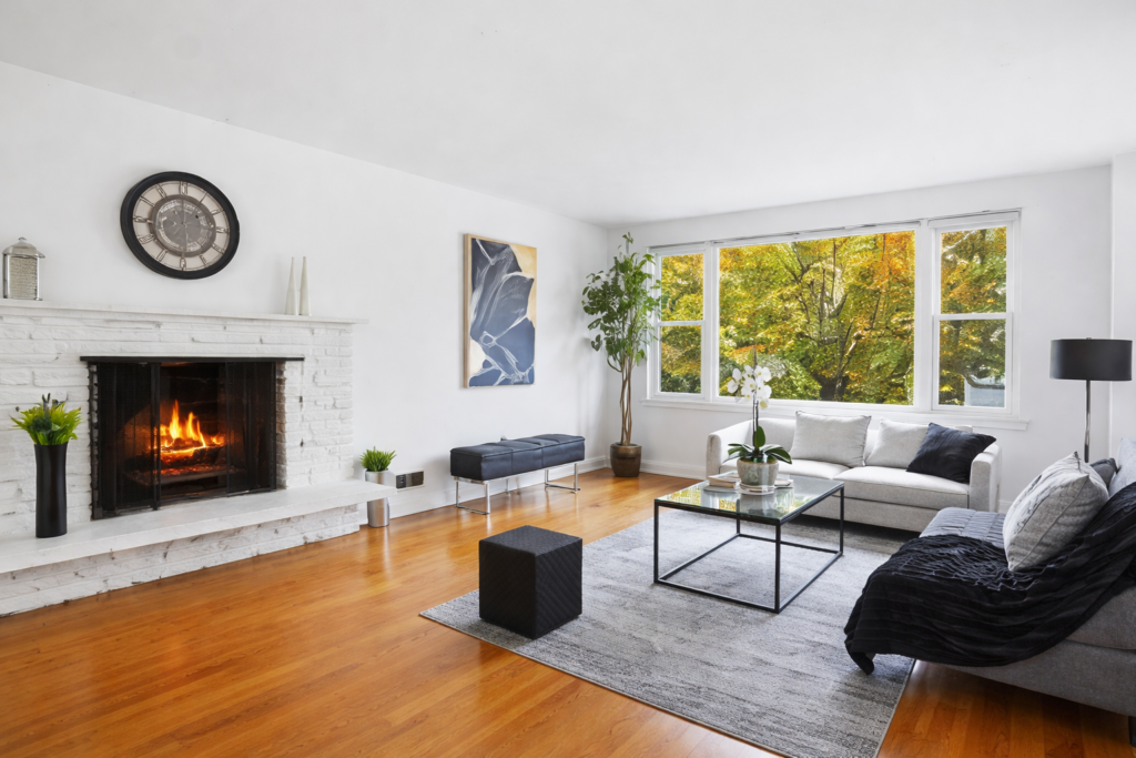 Bright living room with white brick fireplace, large windows, hardwood floors, and modern neutral furniture