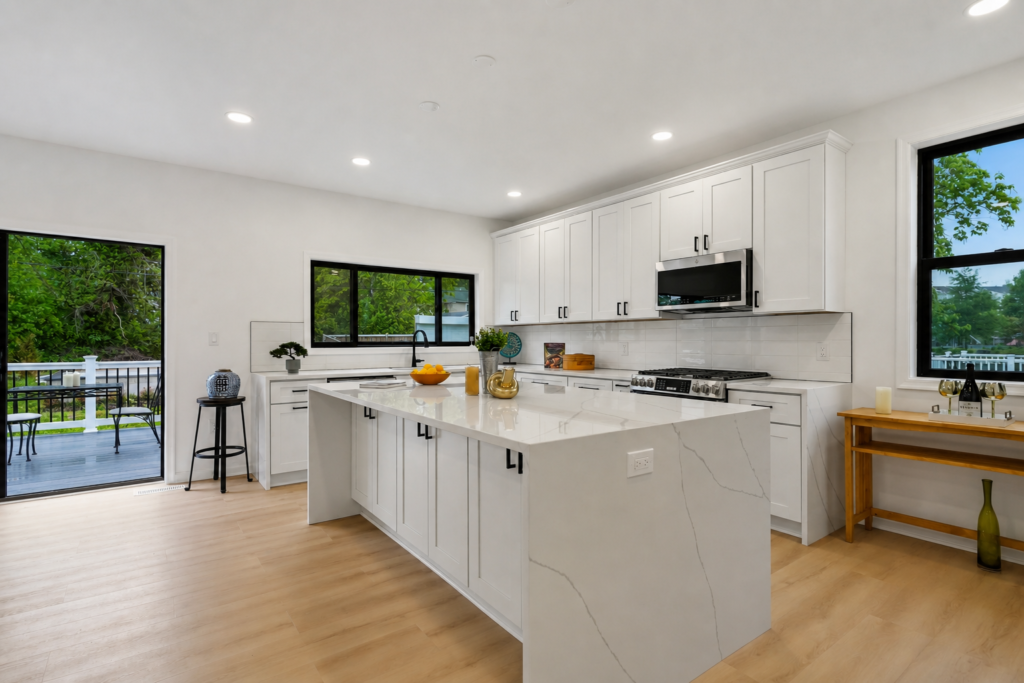 modern white kitchen with large island, light wood floors, and black framed windows