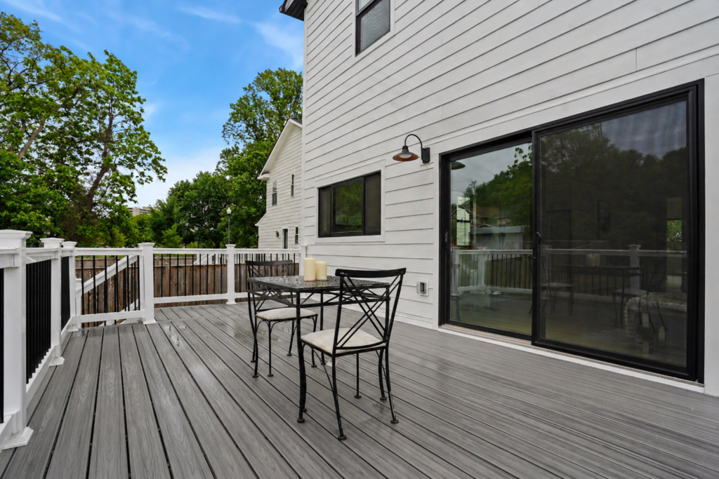 outdoor deck with gray flooring, black metal table and chairs, and sliding glass door