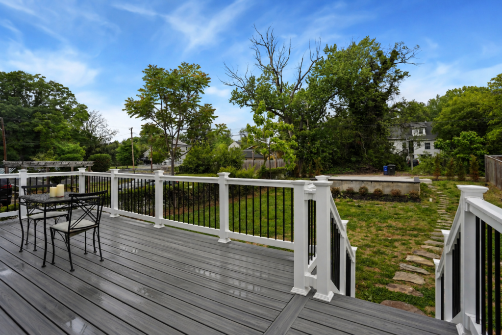 elevated backyard deck with white railing, black seating set, and view of yard and trees
