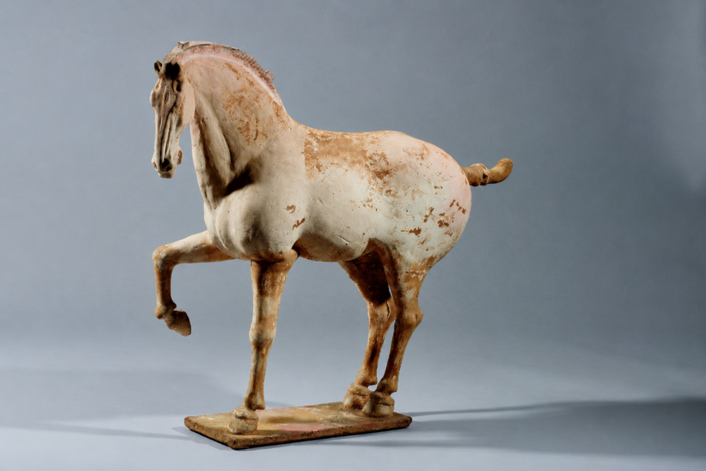 Antique prancing horse sculpture with aged patina on a gray studio background