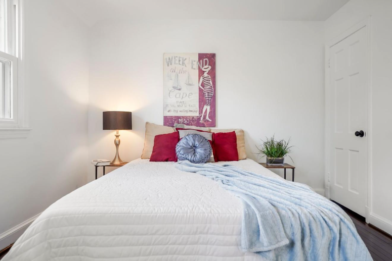 Staged Primary Bedroom Washington DC Harvard Home Services Professionally staged primary bedroom in Washington DC with layered bedding red accent pillows and warm lamp