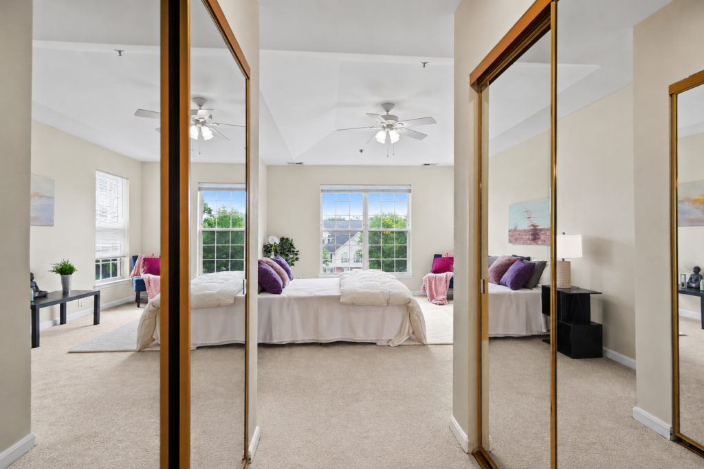 Bright bedroom with mirrored closet doors, large windows, neutral decor, and natural light