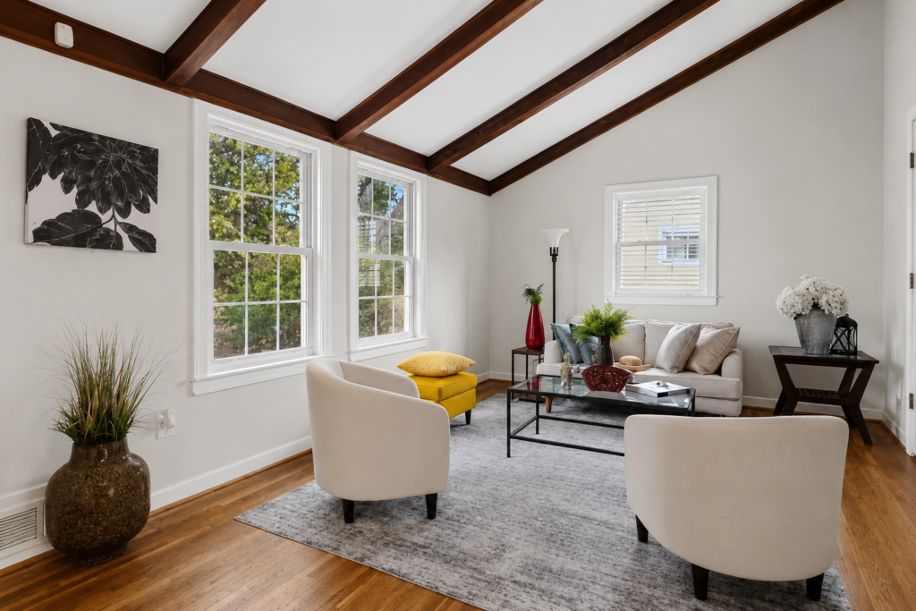 Bright living room with vaulted ceiling, exposed wood beams, large windows, and modern neutral furniture