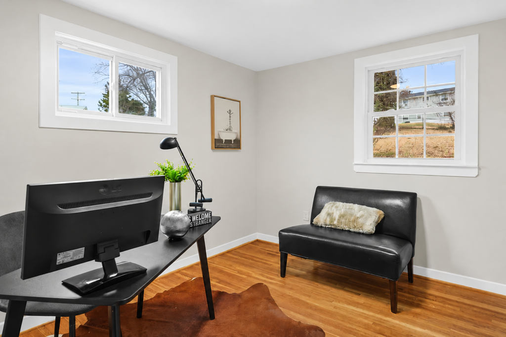 Modern home office with desk, computer monitor, hardwood floors, and natural light from two windows