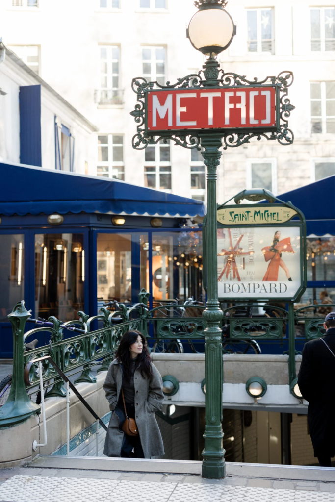Paris Metro Saint Michel entrance with ornate iron work and woman walking in Paris France